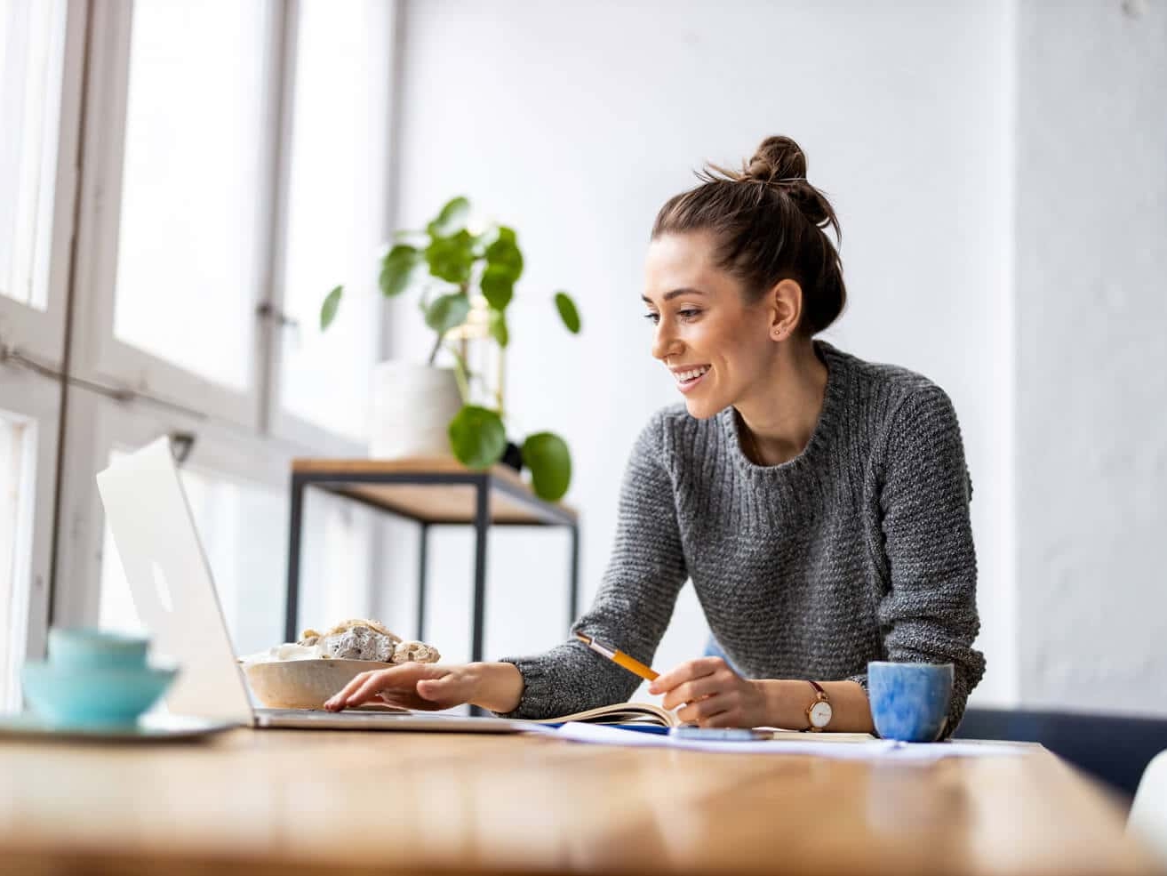 Woman smiling while working on a WordPress website on her laptop in a bright room with food nearby.