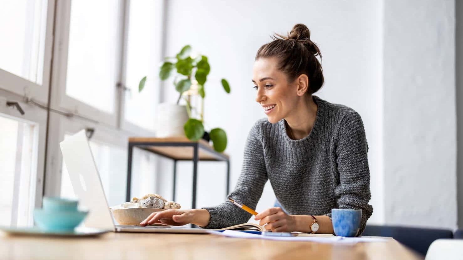 Woman smiling while working on a WordPress website on her laptop in a bright room with food nearby.