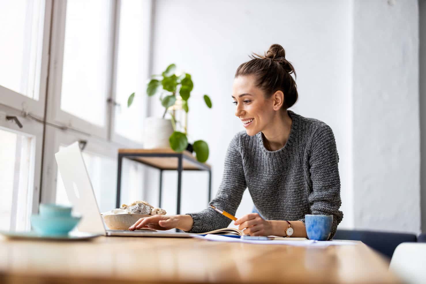 Woman smiling while working on a WordPress website on her laptop in a bright room with food nearby.