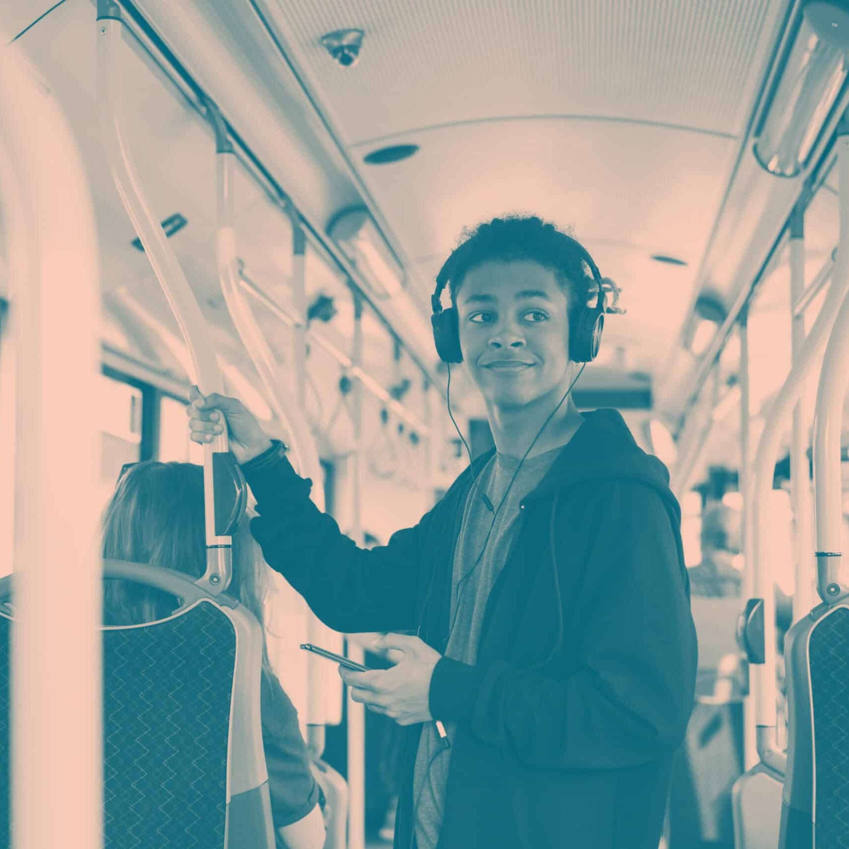 A person standing inside a Colchester bus, wearing headphones and holding a phone, smiles while looking to the side.