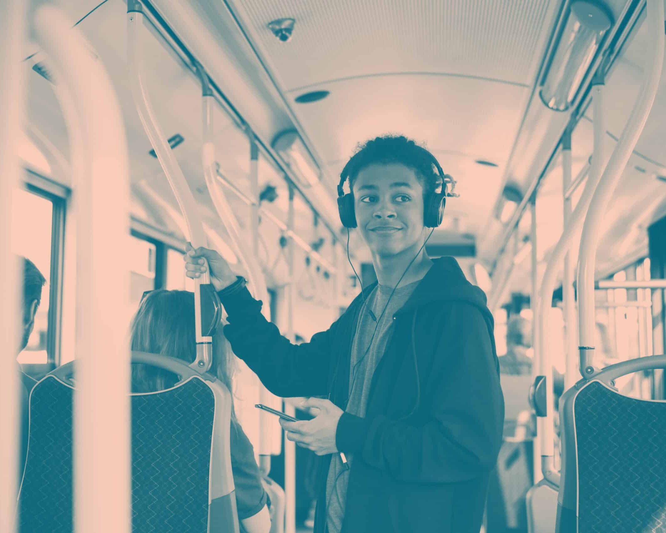 A person standing inside a Colchester bus, wearing headphones and holding a phone, smiles while looking to the side.