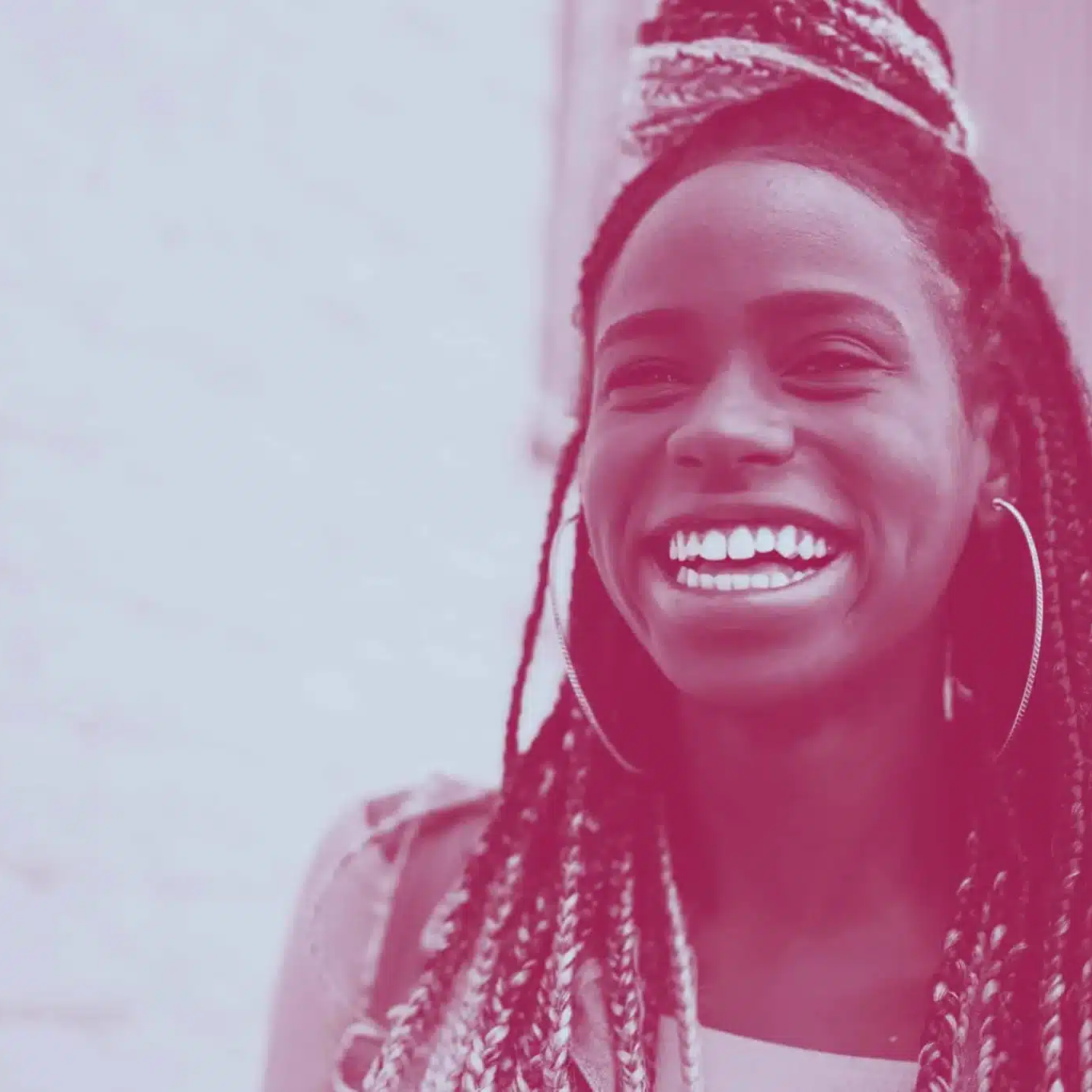 A person with long braided hair and hoop earrings smiles widely, standing outdoors in Colchester against a blurred background, perhaps after visiting the local Citizens Advice Bureau.