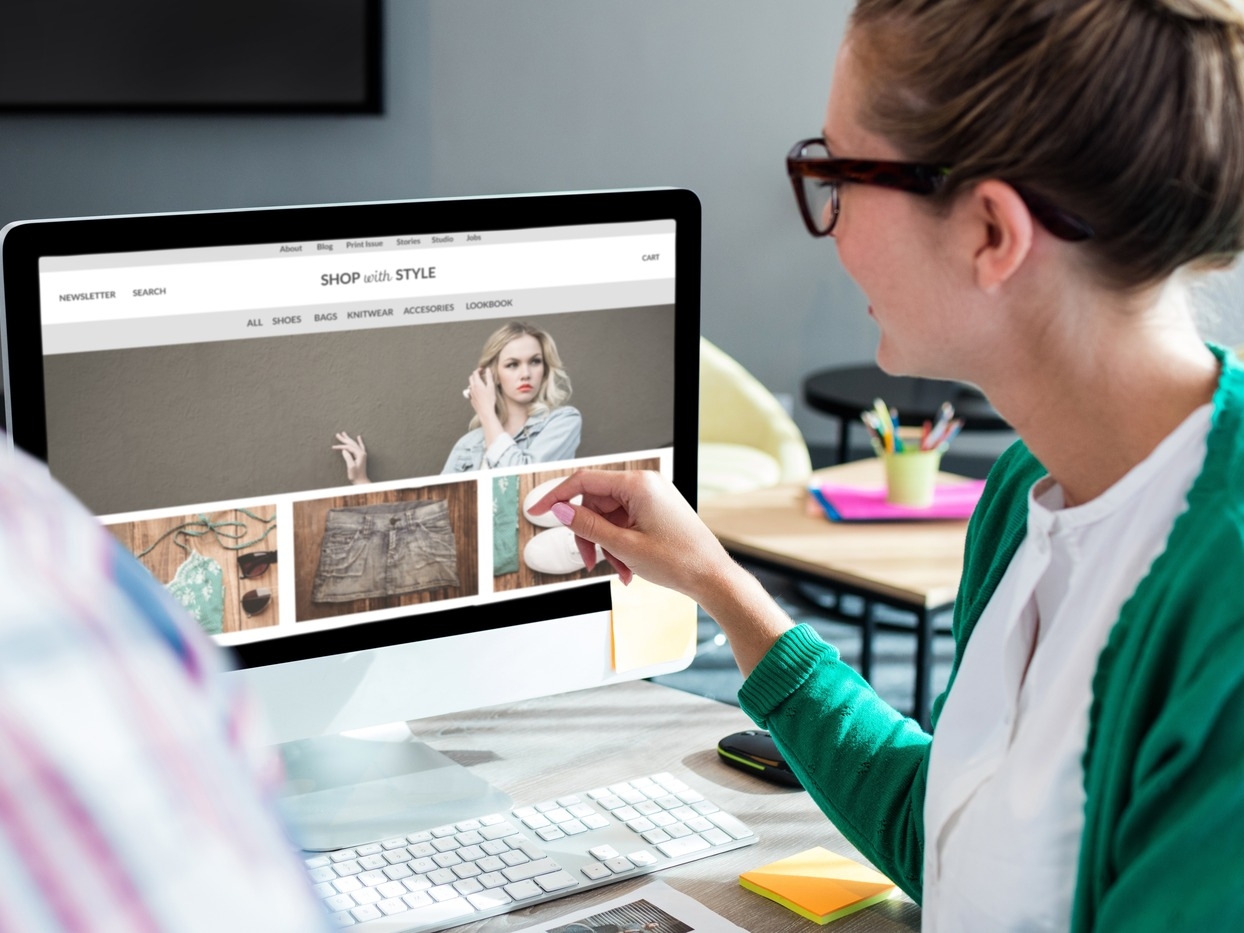 Two people sit at a desk looking at a computer screen displaying an online fashion store, showcasing stylish web design Essex is known for, with a curated selection of clothing and accessories.