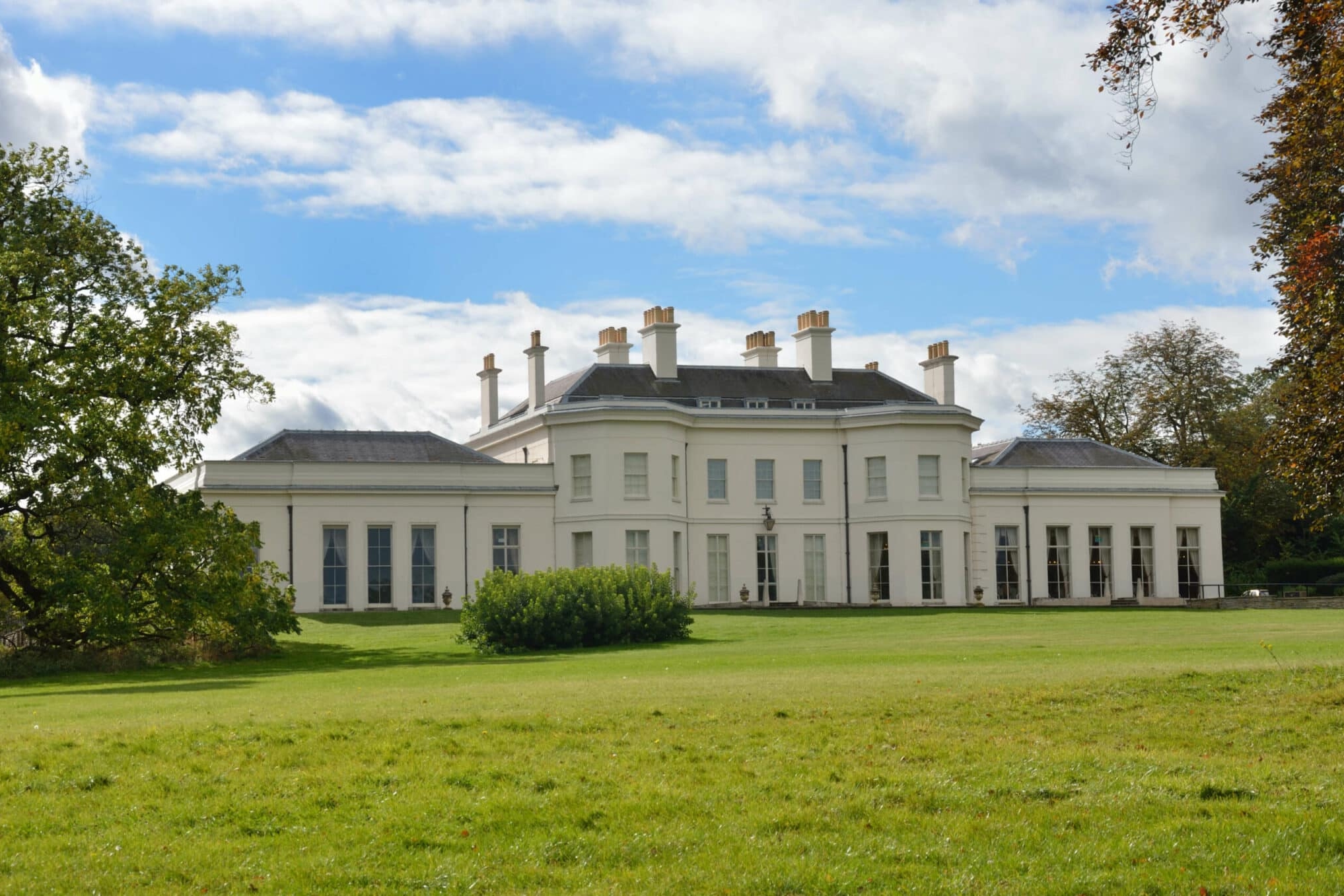 Large white mansion with multiple chimneys, set on a spacious green lawn with trees under a partly cloudy sky—presented by Balch Estate Agents.