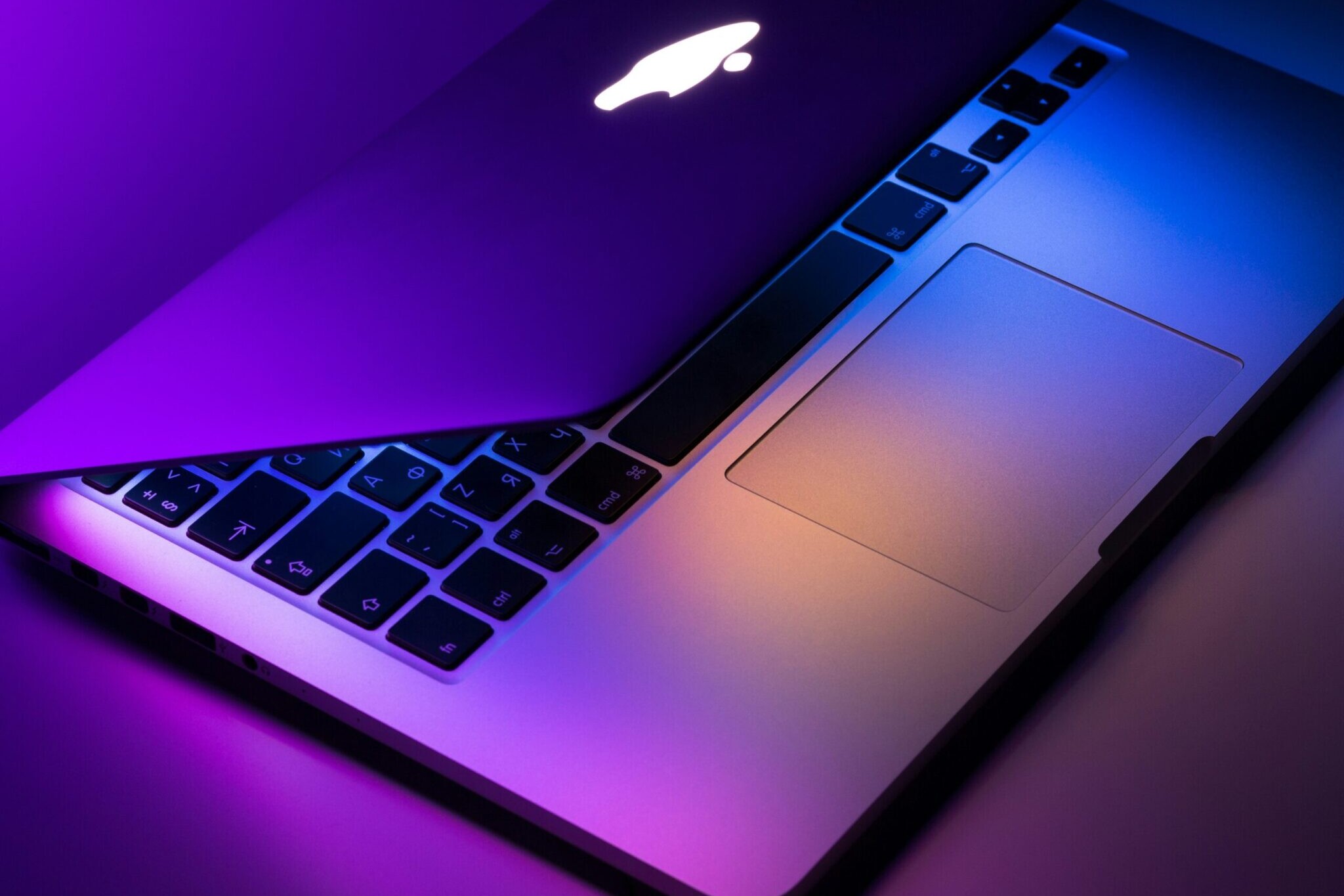 A partially open MacBook laptop with illuminated keyboard and trackpad, featuring purple and orange lighting reflections—showcasing the expert touch of Hardy Repairs.