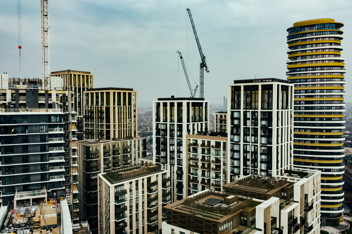 A cluster of modern high-rise buildings and skyscrapers with cranes, some projects managed under Avis Contracts, rises under an overcast sky in an urban cityscape.