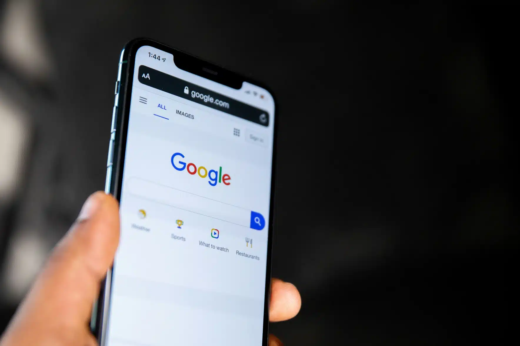 A person holds a mobile phone displaying the Google search homepage on the screen, highlighting the importance of SEO for effective web design.